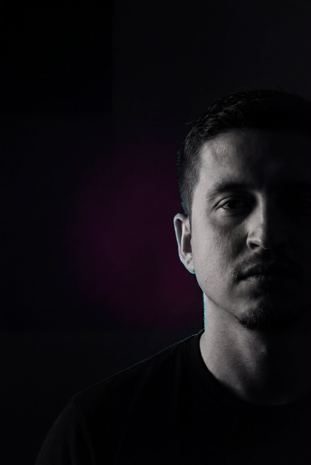 Retrato vertical de Mario Medina con camiseta negra, fondo oscuro y un lado del rostro iluminado.