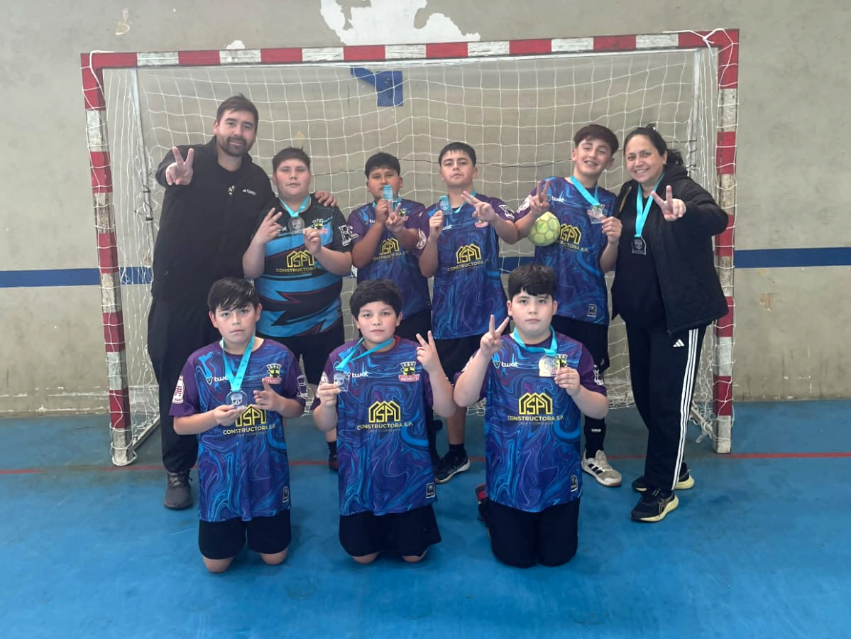 Integrantes del equipo Mini Varones de Balonmano Nacimiento muestran sus medallas frente al arco de una cancha.