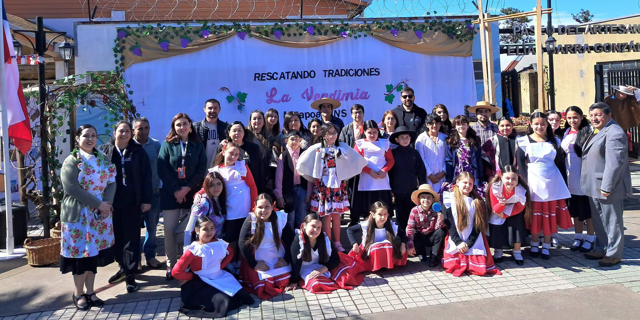 Estudiantes y adultos de la comunidad educativa NNS reunidos frente a la escenografía de la vendimia.