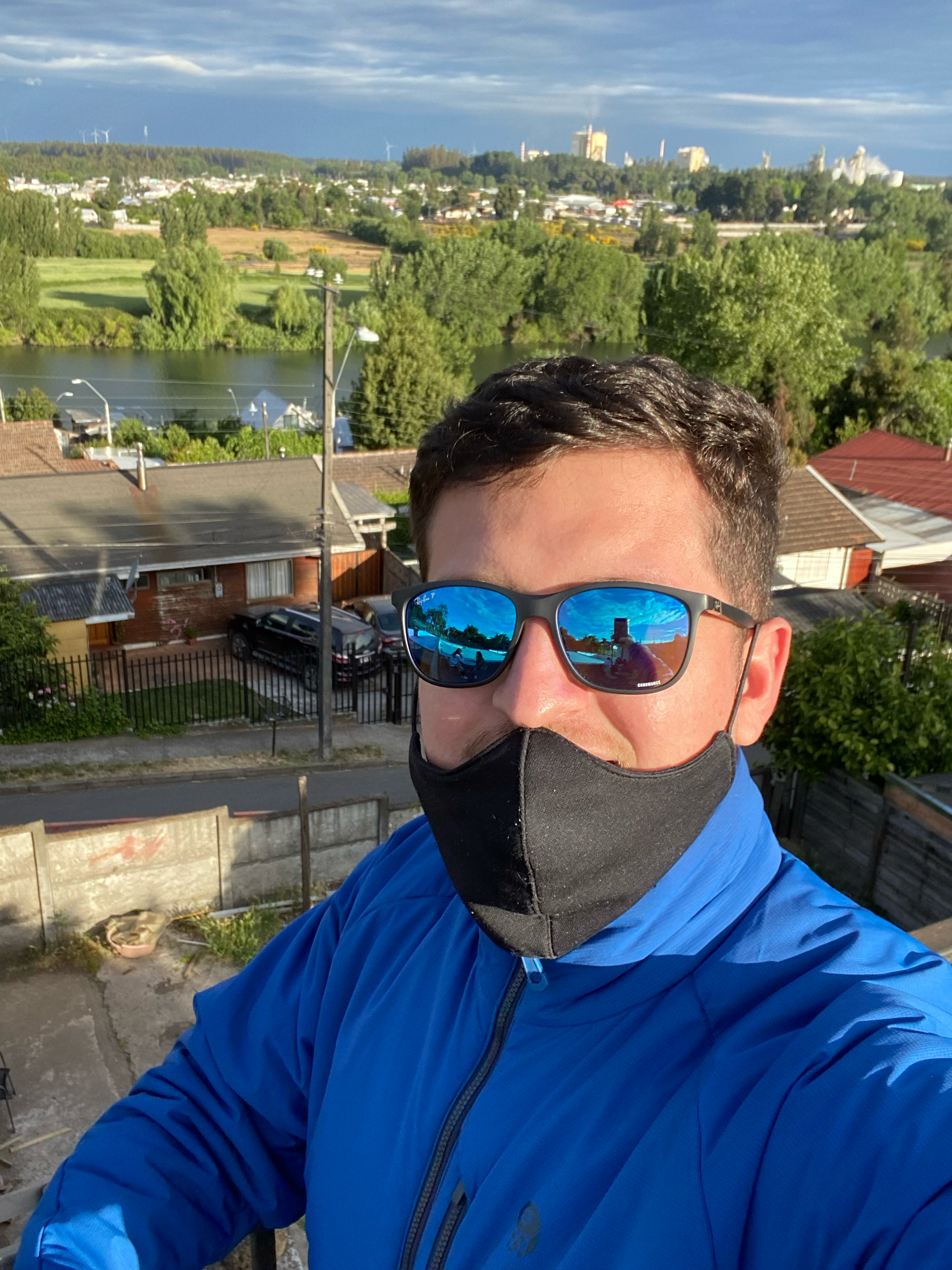 Selfie de Mario Medina con gafas, mascarilla y chaqueta azul; detrás se observan un río, árboles y viviendas.