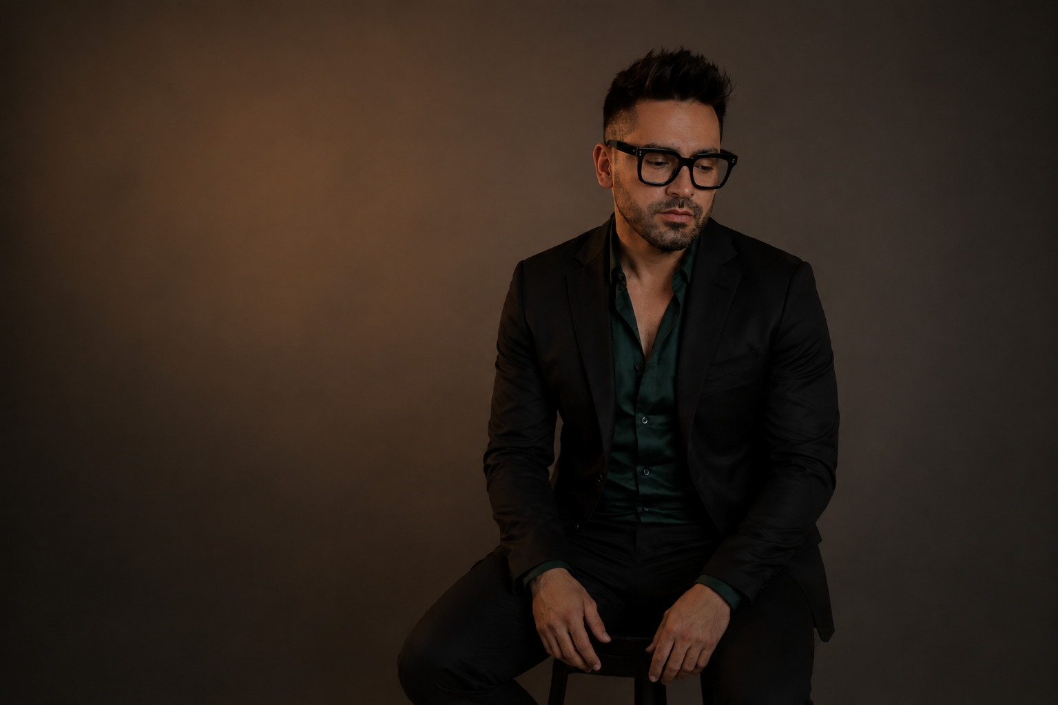 Retrato de Alejandro Shir vestido de negro y sentado frente a un fondo marrón de estudio.