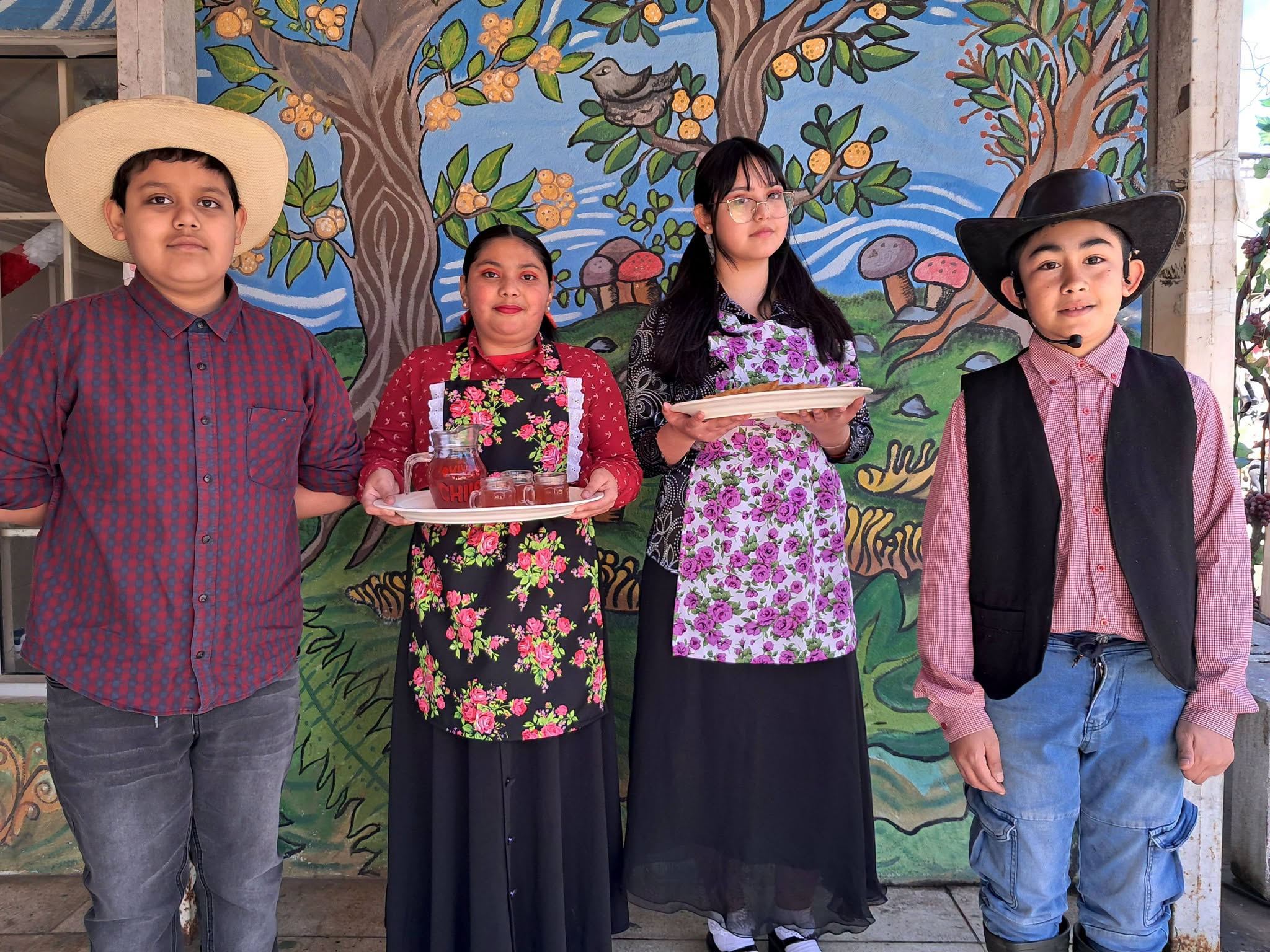 Cuatro estudiantes de séptimo básico con vestuario de la representación de la vendimia posan frente a un mural.